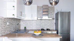 Une cuisine moderne avec des armoires blanches, un réfrigérateur en acier inoxydable, un comptoir en bois et un pare-feu orné d’un motif de mosaïque.