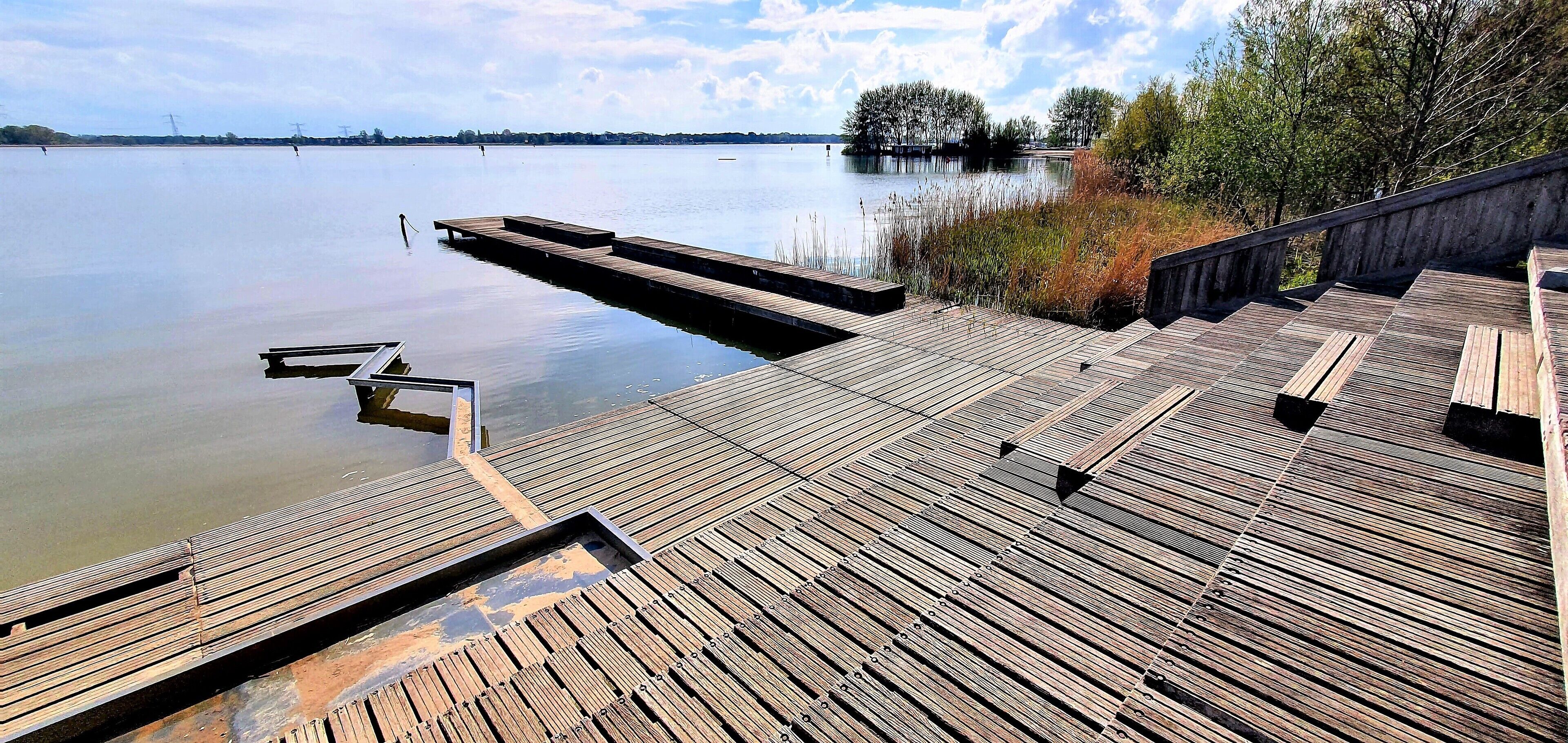 A wooden pier extending into a calm lake with a clear sky above.