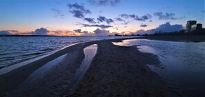 Een strand met nat zand en een ondergaande zon.