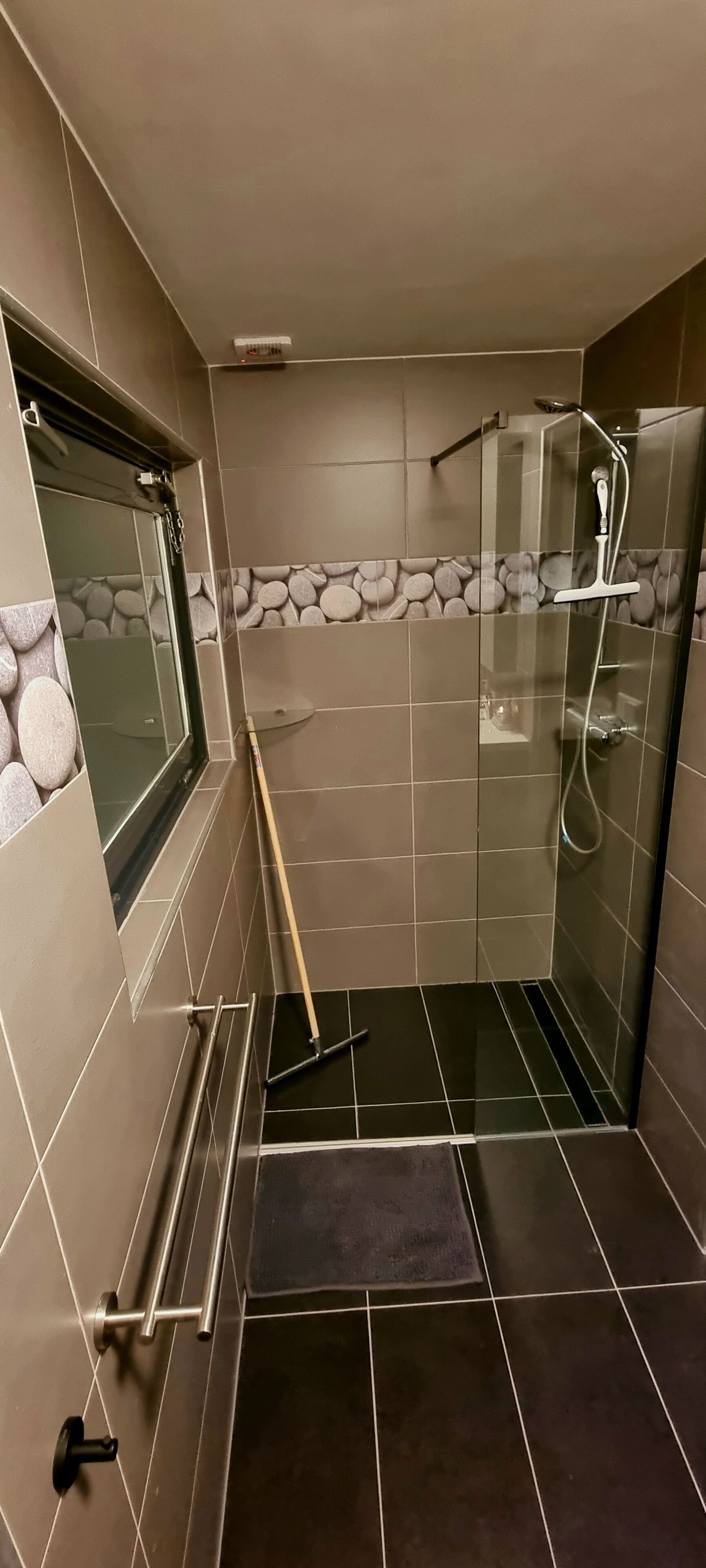 Un espace douche moderne doté d’une porte en verre, d’une barre d’appui, d’une fenêtre et d’un mur en pierre en guise de pare-éclaboussures.