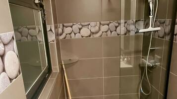 Un espace douche moderne doté d’une porte en verre, d’une barre d’appui, d’une fenêtre et d’un mur en pierre en guise de pare-éclaboussures.