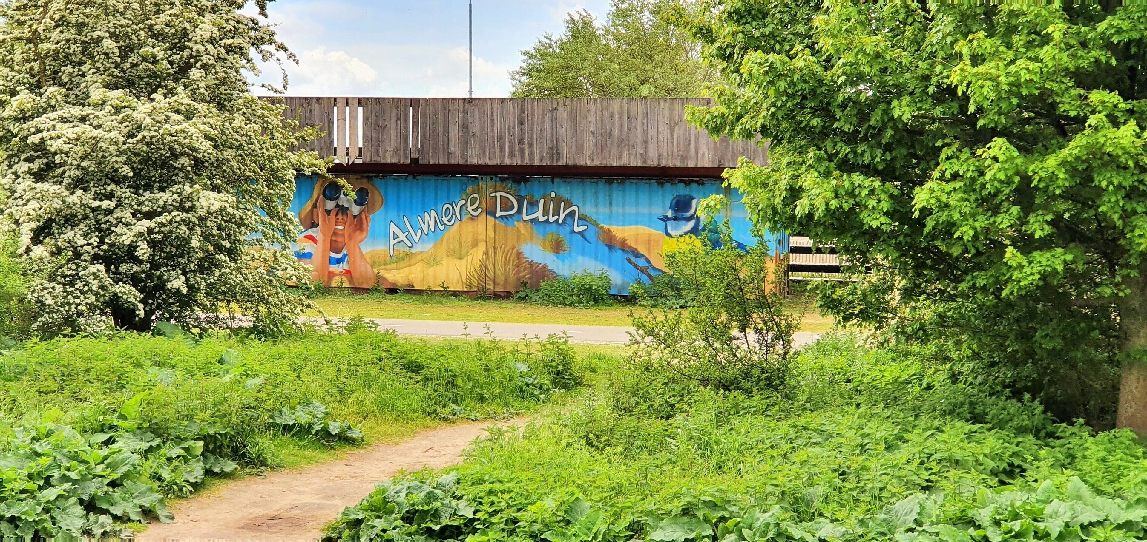 A mural on a wooden structure with greenery in the foreground.