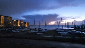 A marina with boats docked, a building with illuminated windows, and a sunset in the background. - Brand new apartment, next to Amsterdam and Floriade 2022, free parkingspace. (Almere)