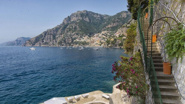 Vista sulla costa con una scala che conduce a una piattaforma rocciosa con posti a sedere all'aperto.