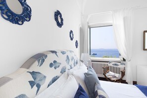 Un dormitori amb llit, finestra amb vista al mar i miralls decoratius a la paret.