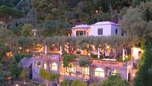 Una villa collinare con diversi livelli, pareti in pietra e una terrazza con posti a sedere all'aperto.