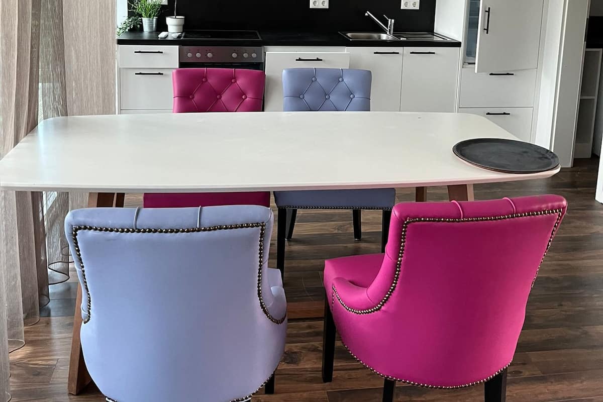 Eine moderne Küche mit weißen Schränken, einer schwarzen Arbeitsplatte und einer eingebauten Mikrowelle. Es gibt einen Esstisch mit zwei Stühlen, einem rosa und einem blauen.
