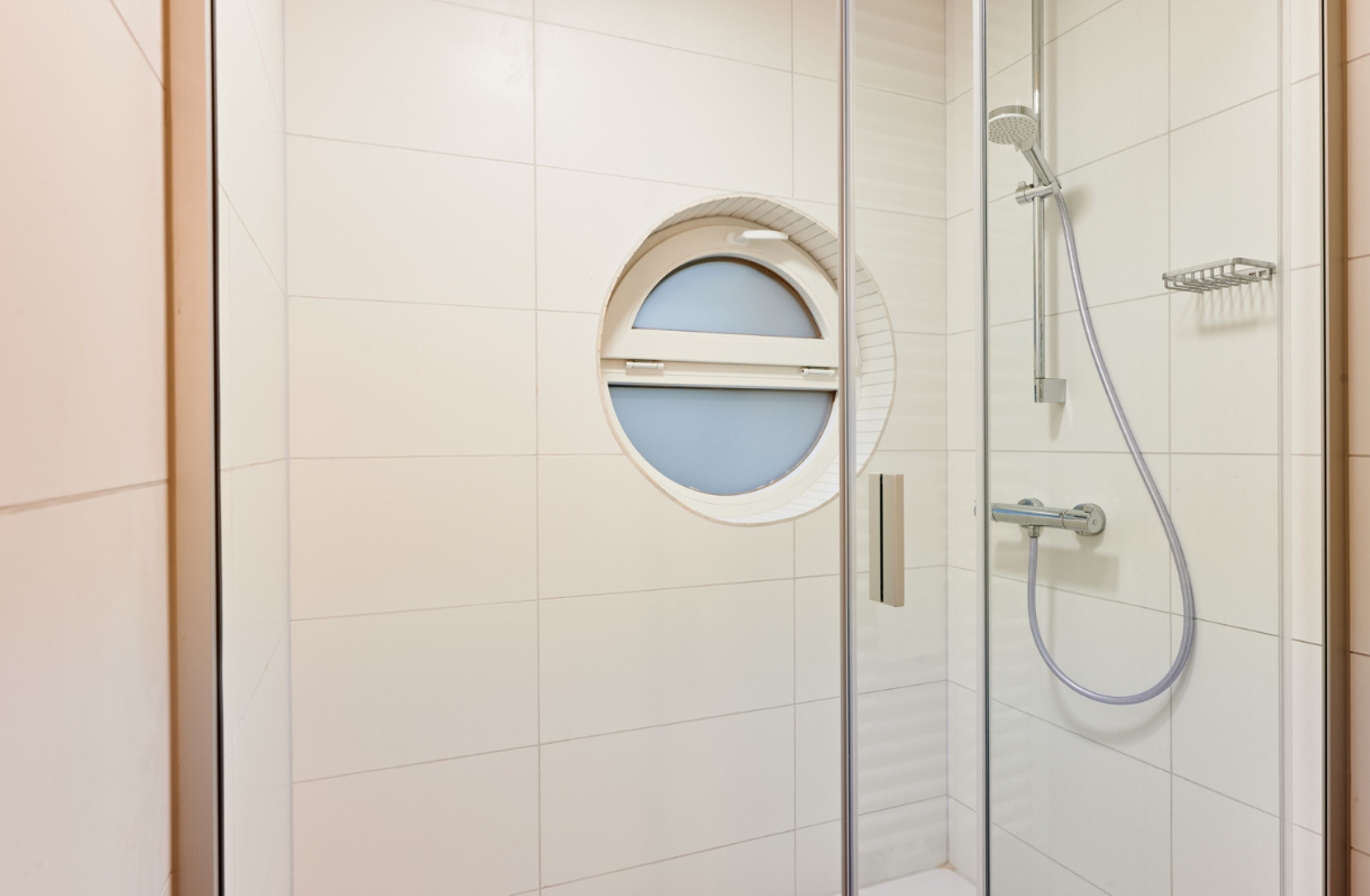 A bathroom with a glass shower enclosure, a round mirror, and a handheld showerhead.