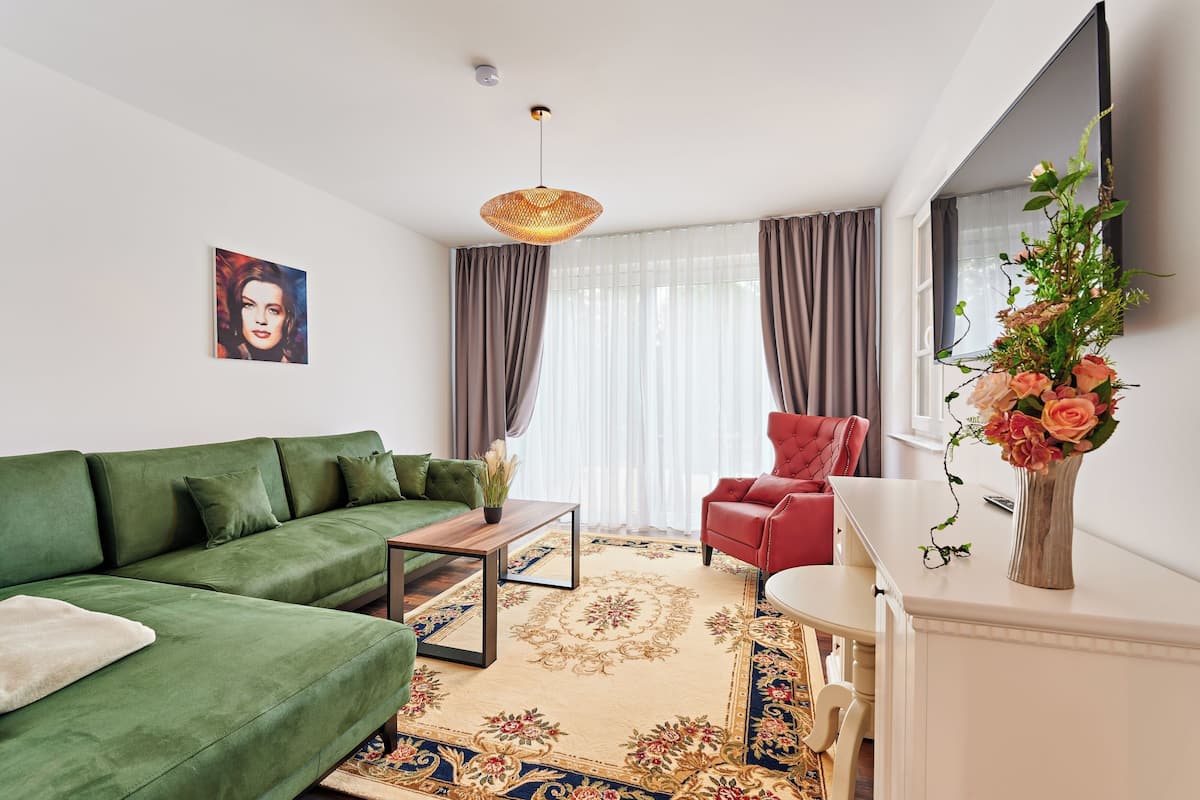 Ein modernes Wohnzimmer mit einem grünen Sofa, einem roten Sessel, einem Holztisch und einem dekorativen Teppich.