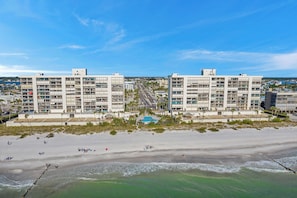A beachfront hotel with multiple floors, a pool, and a beach in the foreground.