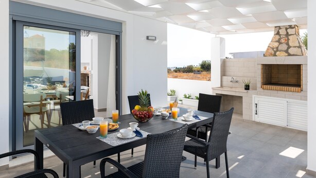 Un área de comedor al aire libre con una mesa dispuesta para el desayuno, una chimenea de piedra y vistas del paisaje.