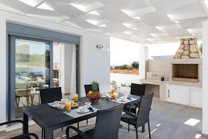 An outdoor dining area with a table set for breakfast, a stone fireplace, and a view of the landscape. - Villa Dama Dama with Private Pool (Kiotari)