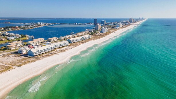 An aerial view of a coastal hotel with beachfront rooms, a pier extending into the ocean, and a clear view of the adjacent beach and water. - Contemporary Gulf Front Townhome Just Steps from the Water (Pensacola Beach)
