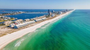 Une vue aérienne d’un hôtel situé sur la côte, avec des chambres donnant sur la plage, une jetée s’étendant dans l’océan et une vue dégagée sur la plage et l’eau adjacentes.