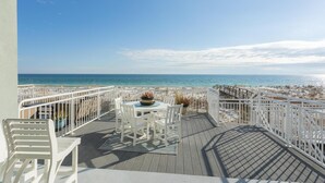 A deck with a table and chairs, overlooking a beach with a railing. - Contemporary Gulf Front Townhome Just Steps from the Water (Pensacola Beach)