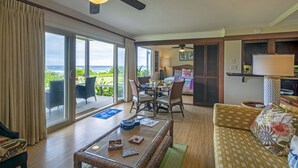 A spacious living area with a dining table, comfortable seating, a ceiling fan, and a view of the ocean through large sliding doors.