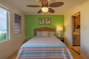 A bedroom with a large bed, a ceiling fan, a view of the ocean, and a wooden cabinet. - Private and Romantic Seaside Retreat - Just Twelve Steps to the Beach! (Hanalei)