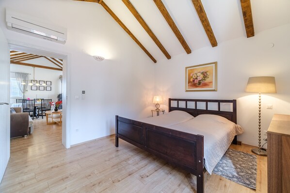Une chambre avec un lit en bois, une lampe de chevet, un tableau au mur et, au fond, un coin repas.