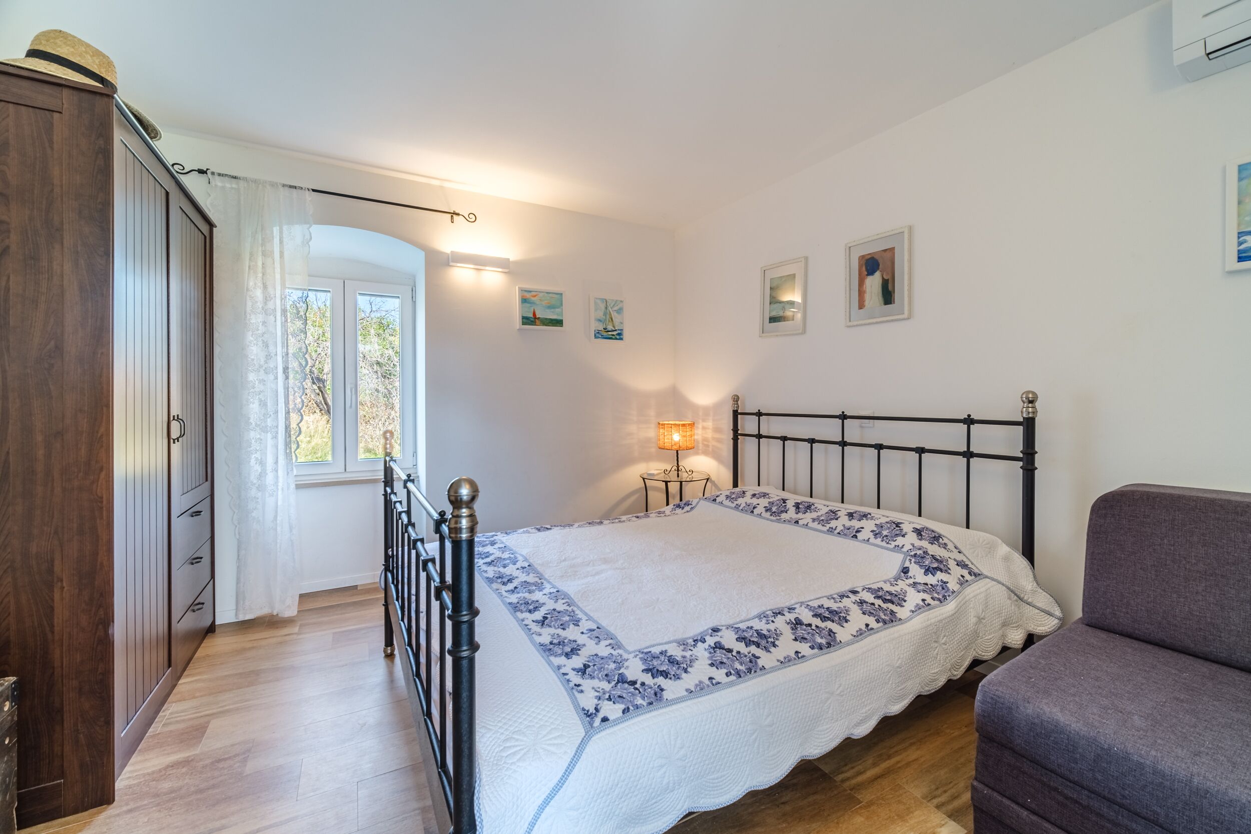 Een slaapkamer met een bed, een kledingkast, een raam met gordijnen, een bedlampje en wanddecoratie.