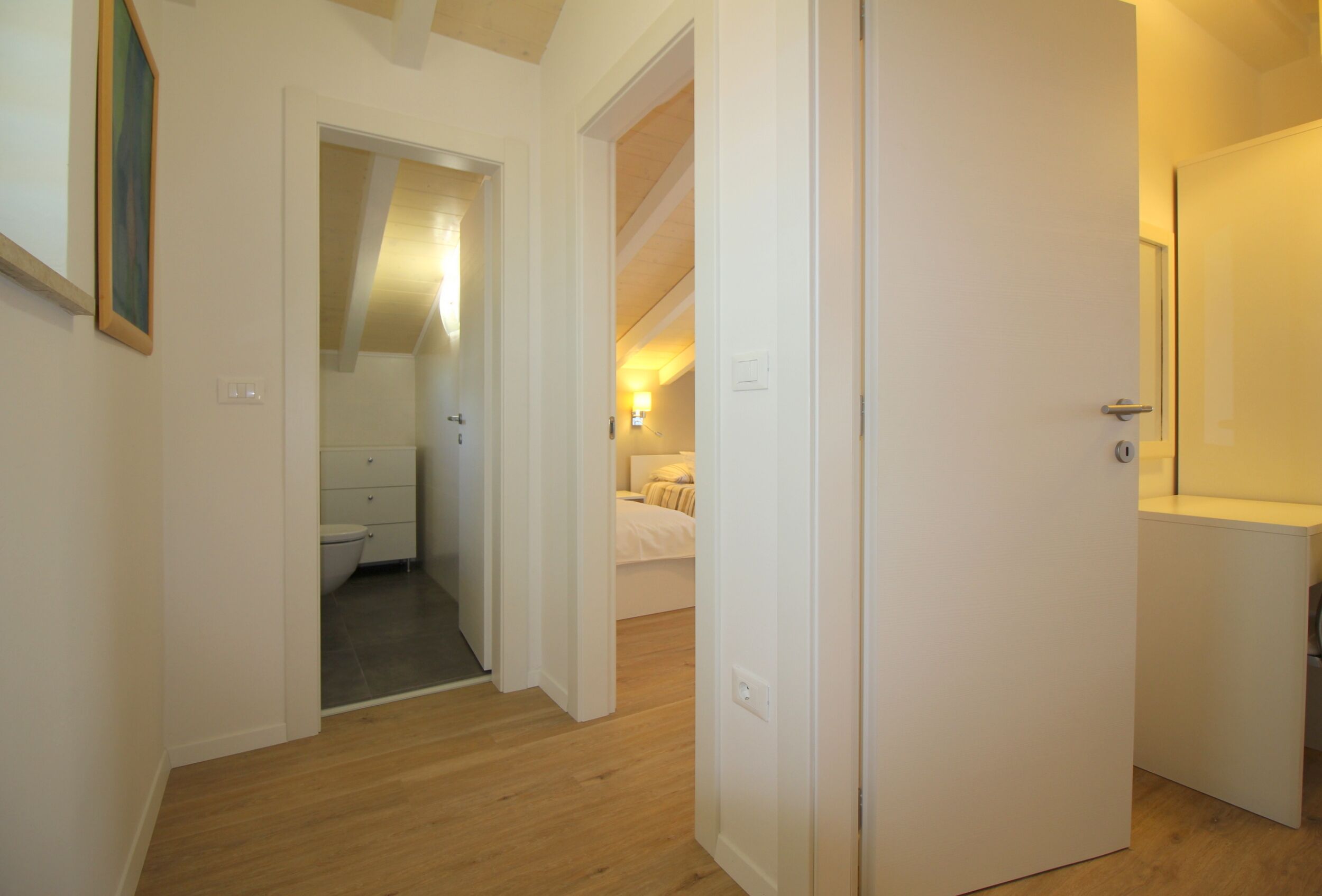 A hallway leading to a bathroom and a bedroom with a bed and bedside table.