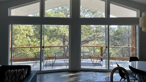 Una habitación amplia con ventanas grandes, un balcón con mobiliario exterior y vistas a árboles.