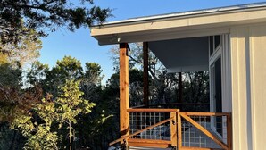 Un edificio moderno con fachada de hormigón, una escalera de madera que lleva a un porche cubierto y vistas a árboles circundantes.