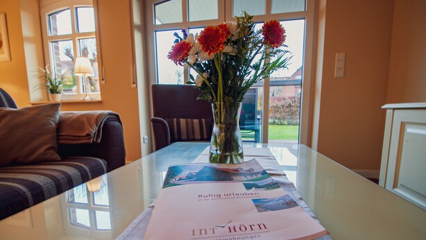 Une table avec une brochure, un vase de fleurs et une vue sur l’extérieur.