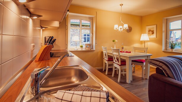 A modern kitchen with a stainless steel sink, wooden countertop, and a dining area with a table and chairs. - Int Hörn 1 EG (Krummhörn)