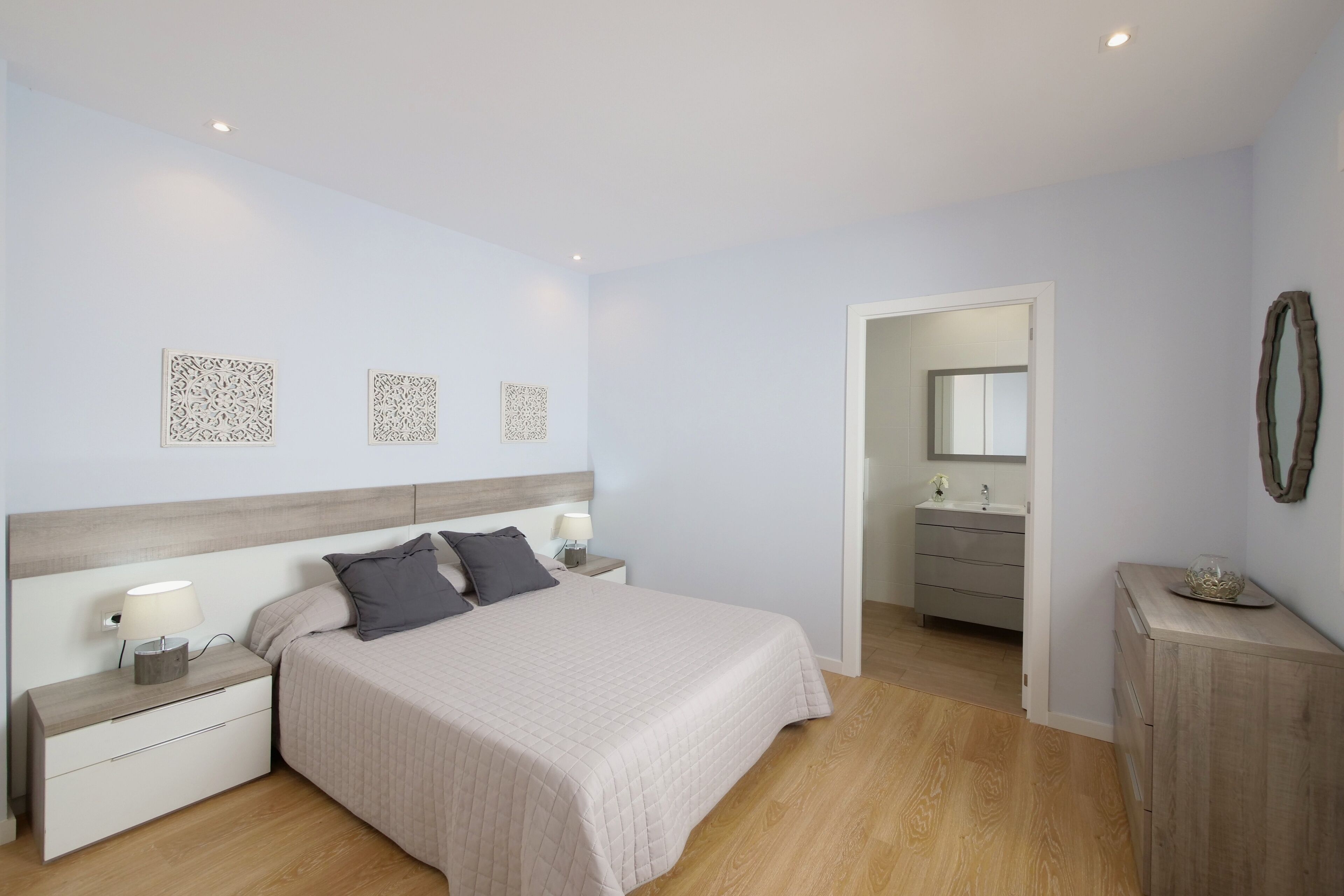 Une chambre à coucher avec un lit, des tables de chevet, une commode et une salle de bain visible à travers une porte ouverte.