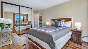Un dormitorio con una cama grande, una mesita de noche de madera, un espejo y vistas al exterior.