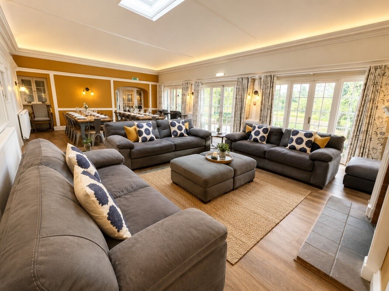 A spacious living room with a high ceiling, a dining area with a table set for six, and large windows with curtains.