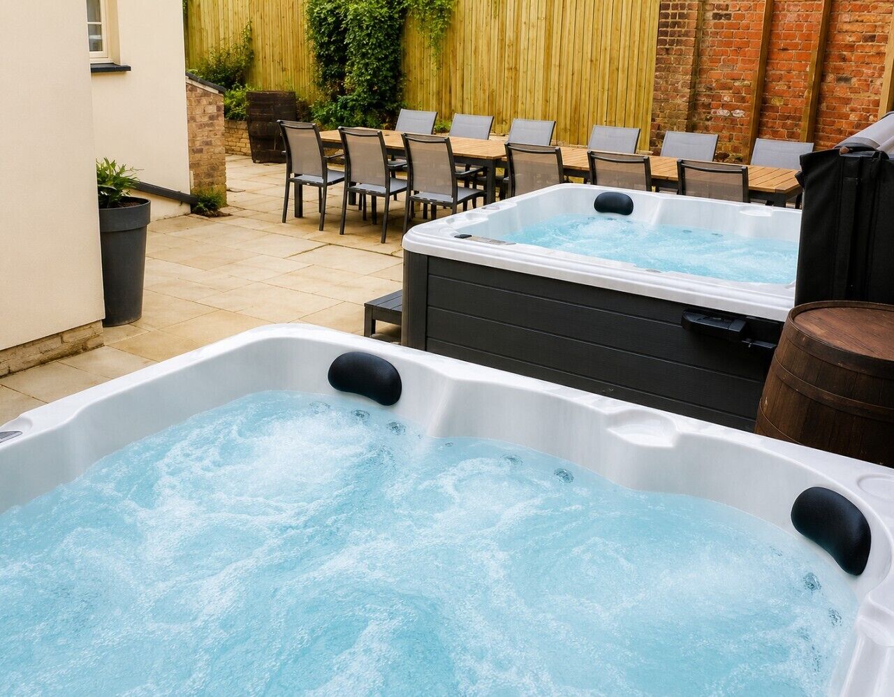Dos jacuzzis en un patio exterior con un muro de ladrillo y una valla de madera al fondo.