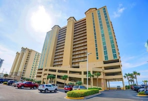 Un hotel de varios pisos con garaje, palmeras y cielo despejado.