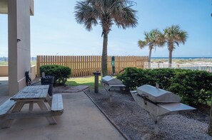 An outdoor patio area with a wooden table and benches, a barbecue grill, and a view of the beach and ocean. - 3BR Gulf Front Condo | Sleeps 8 | Breathtaking Views (Gulf Shores)
