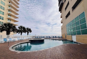 A swimming pool with lounge chairs, a brick patio, and a building with balconies. - 3BR Gulf Front Condo | Sleeps 8 (Gulf Shores)