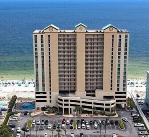 A multi-story hotel with a central courtyard, parking lot, and a view of the beach.