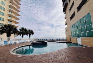 Une piscine avec des chaises longues, une terrasse en briques et un bâtiment doté de balcons.