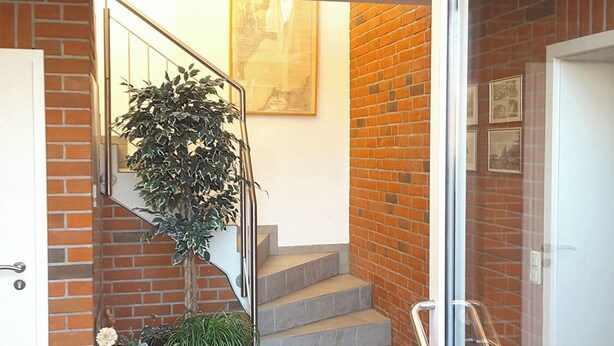 A staircase with a glass door leading to a room, a potted plant, and a small table with a basket and flowers. - Quietly situated apartment for max. 4 persons, balcony, garden, WLAN, washing machine (Prerow)