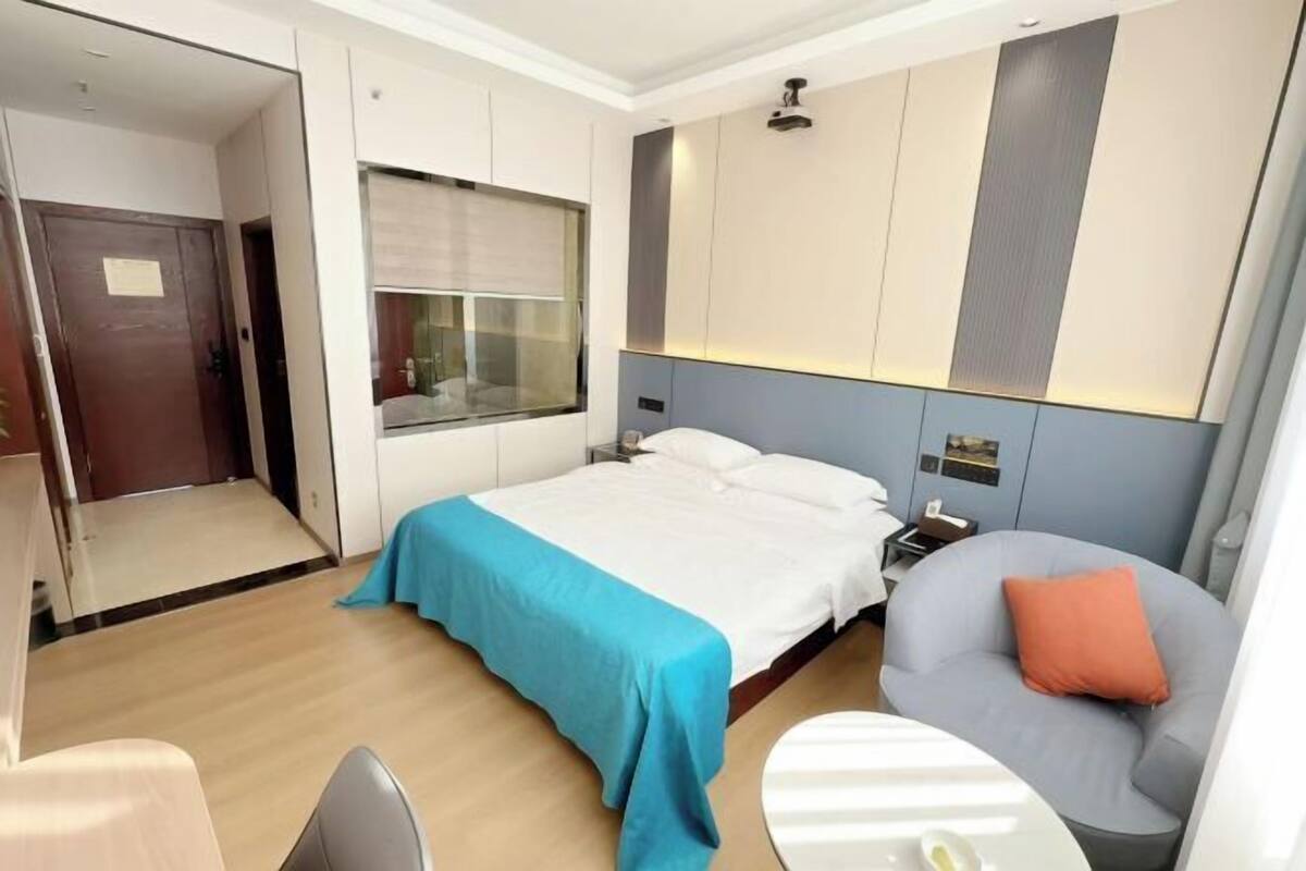 Une chambre d’hôtel avec un lit, une chaise, une petite table, un miroir et une armoire.