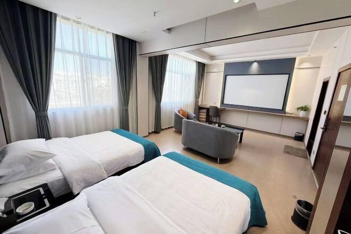 Une chambre d’hôtel avec deux lits, un bureau, une chaise, une télévision et une grande fenêtre.