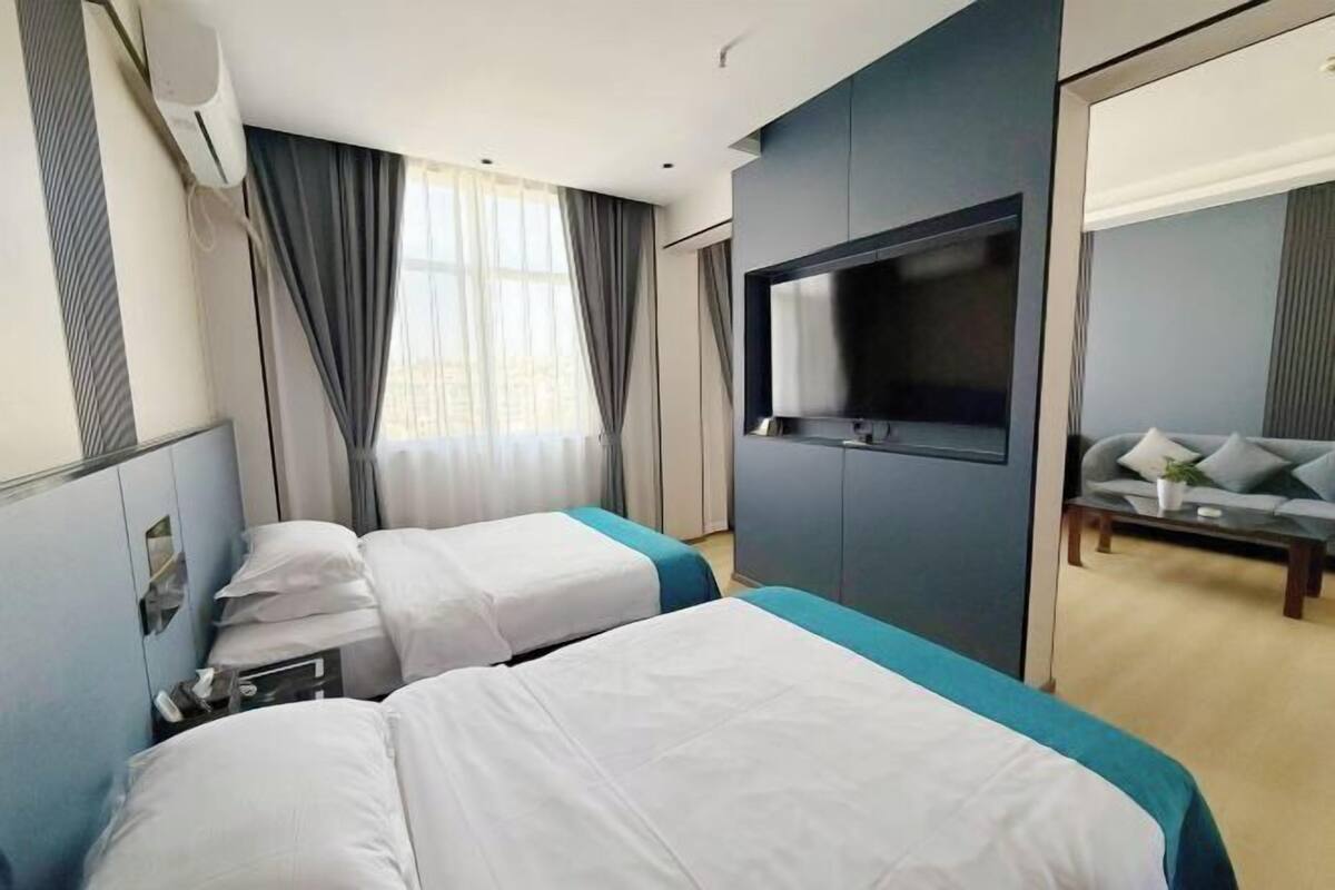 Une chambre d’hôtel avec deux lits, une télévision, un canapé et une grande fenêtre avec des rideaux.