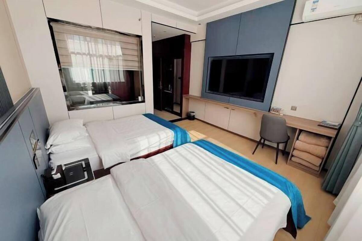 Une chambre d’hôtel avec deux lits, un bureau, une chaise, une télévision et une fenêtre avec des stores.