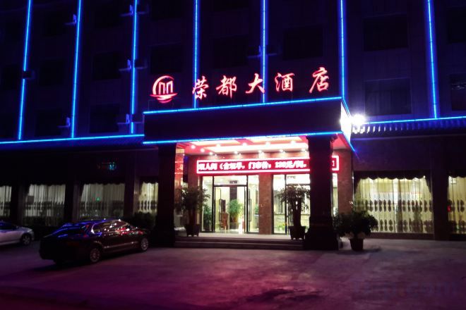 A hotel entrance with a neon sign, a reception desk, and a parking area.