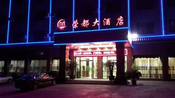 A hotel entrance with a neon sign, a reception desk, and a parking area.
