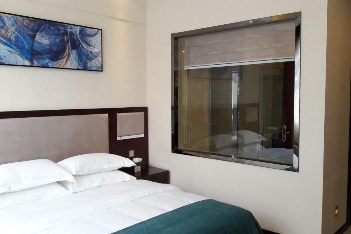 Una habitación de hotel con cama, mesita de noche, un cuadro y ventana con vistas.