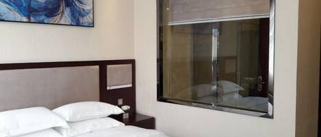 A hotel room with a bed, a nightstand, a painting, and a window with a view.