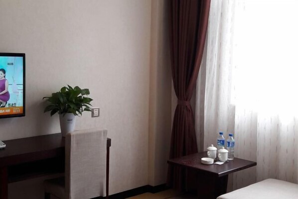 Habitación de hotel con cama, una mesita con botellas de agua, una planta en maceta y un televisor en la pared.