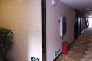 Un pasillo con una planta, un detector de incendios y un cubo de basura rojo.