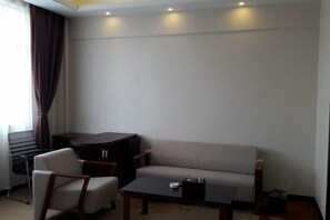 Habitación moderna con sofá, una mesita y una silla. Se observa una ventana con cortinas, un radiador y un cubo de basura.