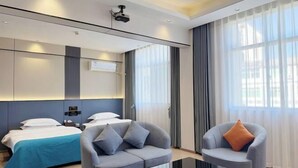 Una camera d'albergo moderna con un letto, due poltrone, un tavolino e una grande finestra con tende.